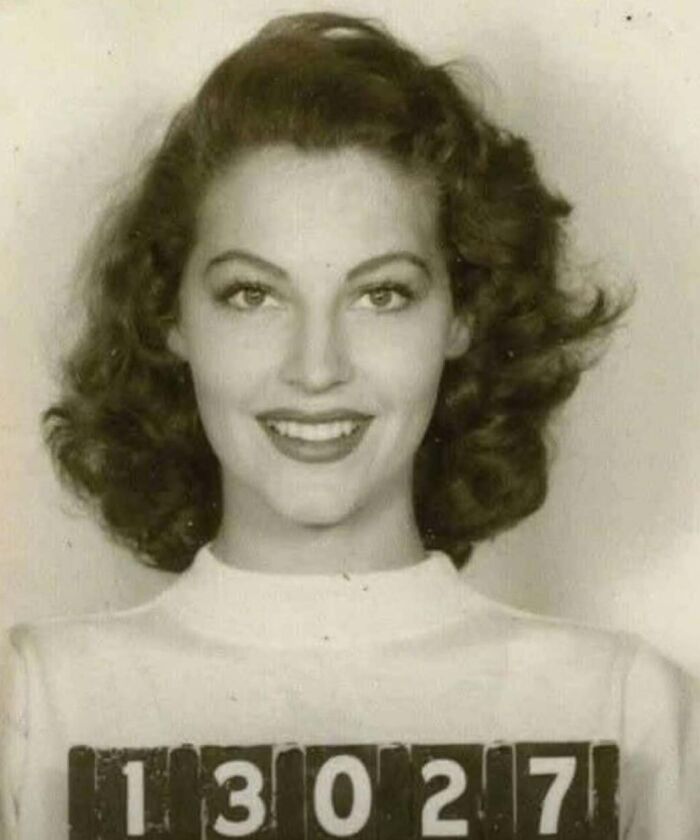 Smiling woman with 13027 sign in black and white, offering a fascinating look into historical photos.