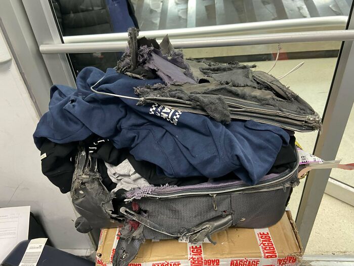 Damaged airline baggage with torn clothing spilling out, illustrating an epic baggage fail at an airport.