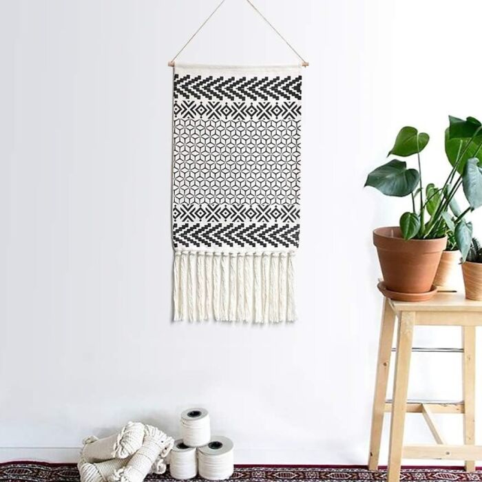 Macrame wall hanging with geometric pattern, a must-have for grown-up 80s kids; decor by potted plants and yarn.