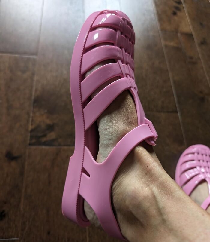 Pink jelly sandals on a person's feet evoke 80s nostalgia on a wooden floor.