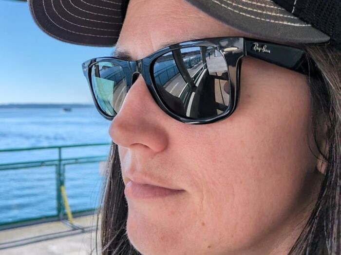 Person wearing sunglasses and a cap on a sunny day, with reflections of water, capturing an 80s nostalgic vibe.