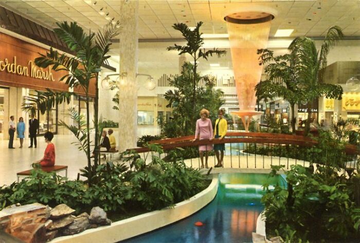 Vintage mall interior with a lush fountain, shoppers, and the Jordan Marsh sign capturing nostalgic architecture.