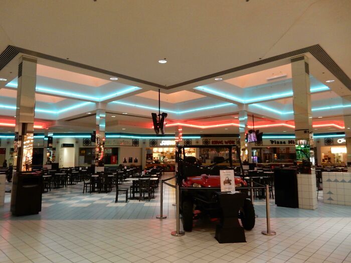 Vintage mall food court with neon lights and empty seating area, showcasing retro dining atmosphere.