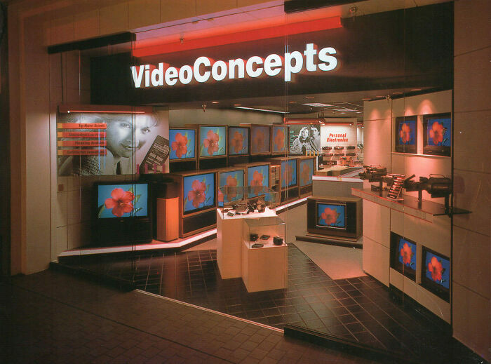 Vintage mall store with VideoConcepts sign, showcasing rows of TVs displaying floral images.
