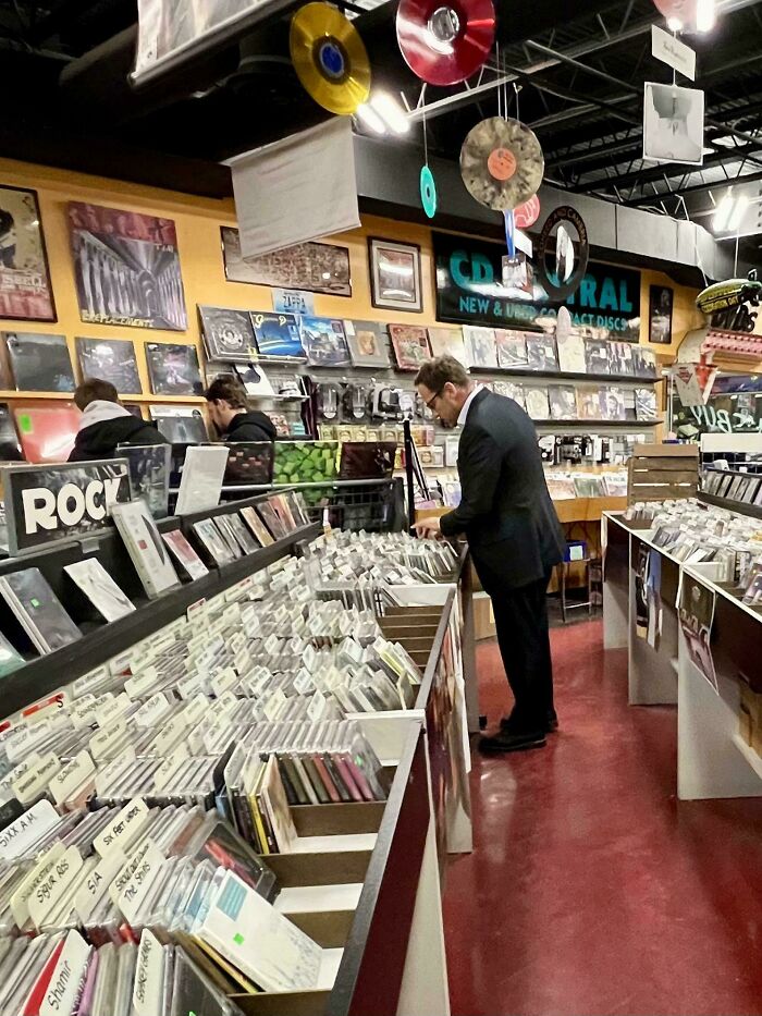 Man browsing CDs in a vintage mall record store, with vinyl records and album covers on display.