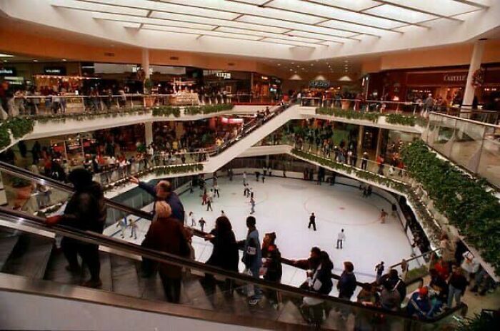 Vintage mall with bustling crowds overlooking an indoor ice rink, capturing the essence of retro shopping experiences.