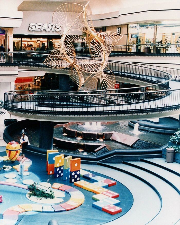 Vintage mall scene with a Sears store, spiral staircase, and colorful play area, capturing nostalgic vibes of the era.