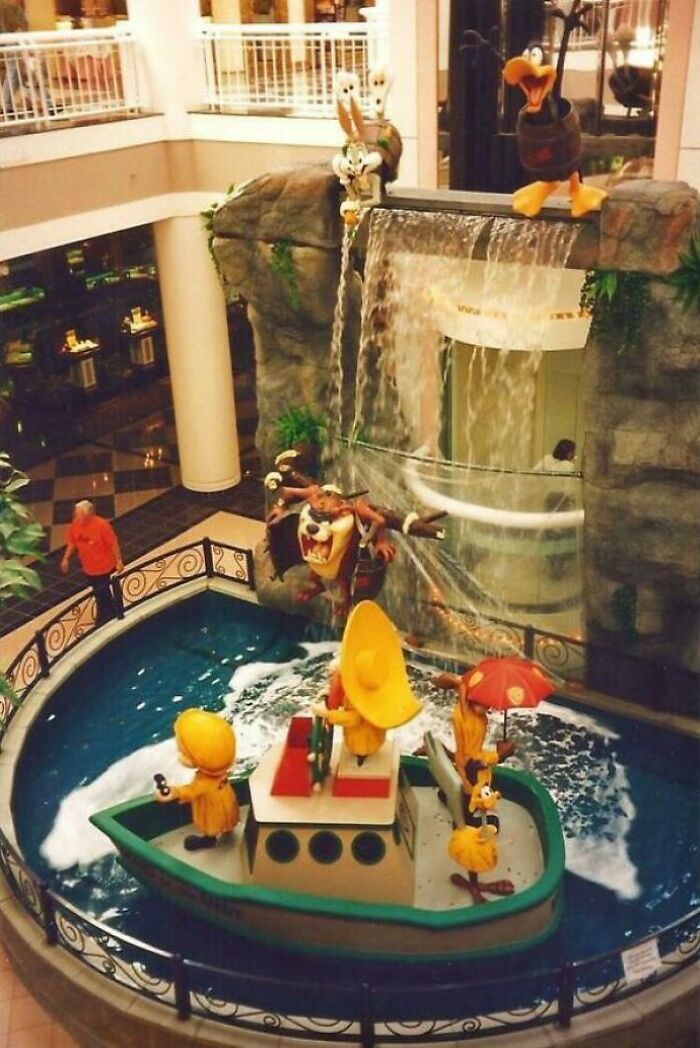 Vintage mall fountain display with cartoon characters in a boat surrounded by water and artificial rock.