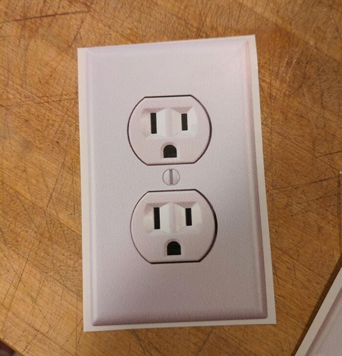 Sticker of an electrical outlet placed on a wooden surface as an April Fools prank.