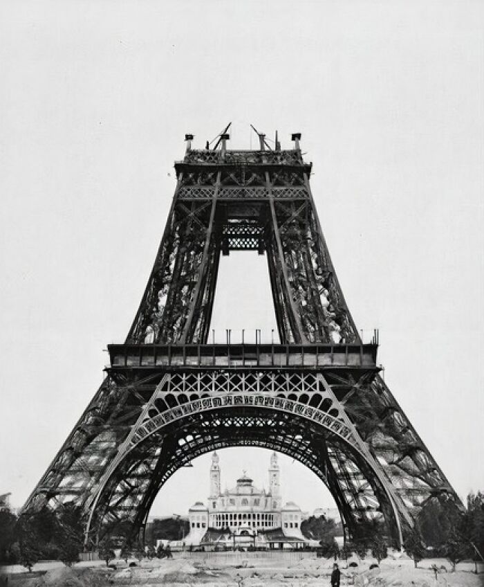 Eiffel Tower under construction with a historic building visible in the background, showcasing iconic architecture.