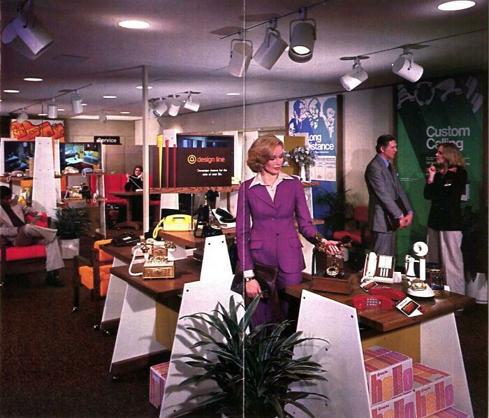 Vintage mall scene with a woman in a purple suit near retro phones, surrounded by people and store displays, evoking nostalgia.