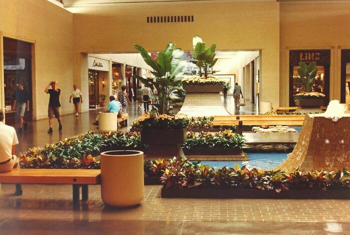 A vintage mall scene with indoor garden and shoppers, evoking nostalgia for classic food courts.