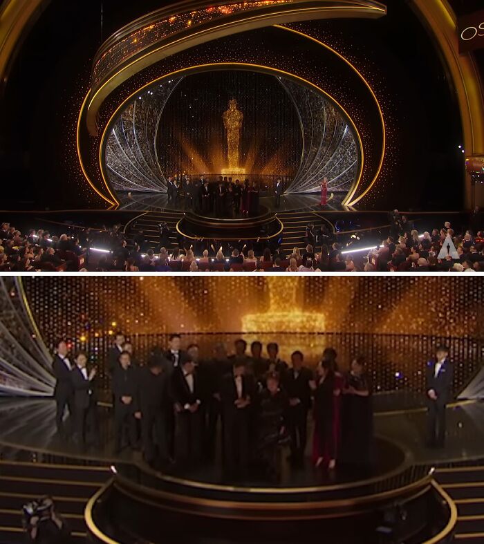 Golden statue center stage at an awards show, audience in seats, group of people on stage during a dramatic moment.