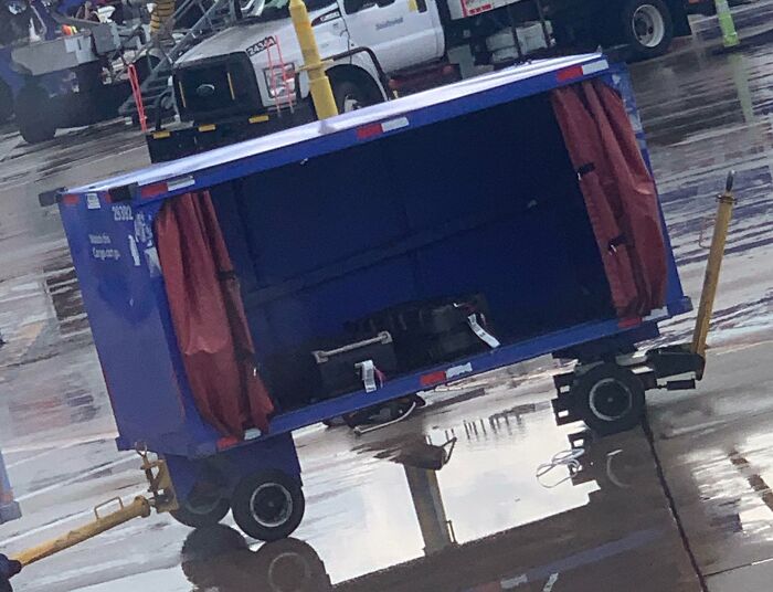 Airline baggage mishap with an open luggage cart on a wet airport tarmac.