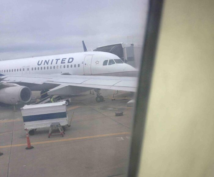 Airline baggage mishap with cargo container stuck under United plane wing at airport gate.