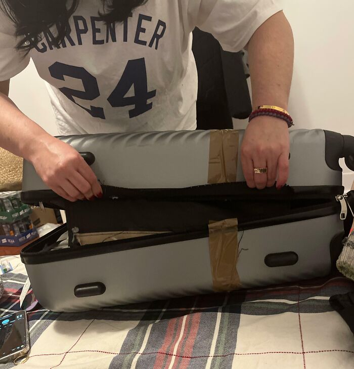 Person inspecting a broken suitcase, reinforced with tape, illustrating airline baggage fails.