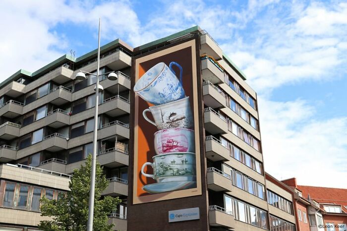 Mind-bending 3D street art of stacked teacups on a building wall under a blue sky.