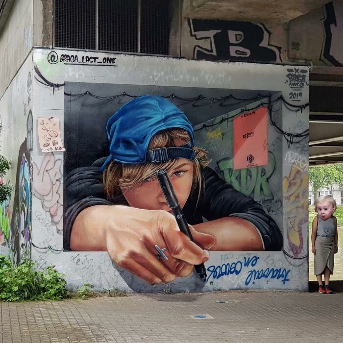 3D street art masterpiece of a person in a blue cap holding a marker, blending into urban graffiti.