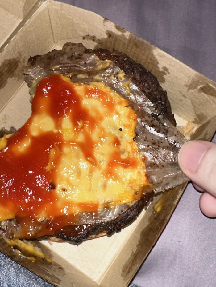 Disgusting burger with melted cheese and sauce, revealing an unappetizing texture in a cardboard box.