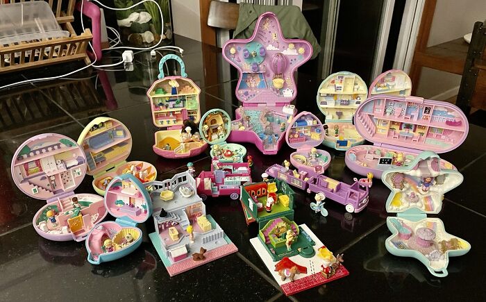 Colorful display of vintage Polly Pocket compacts and playsets, showcasing their intricate designs on a black tabletop.