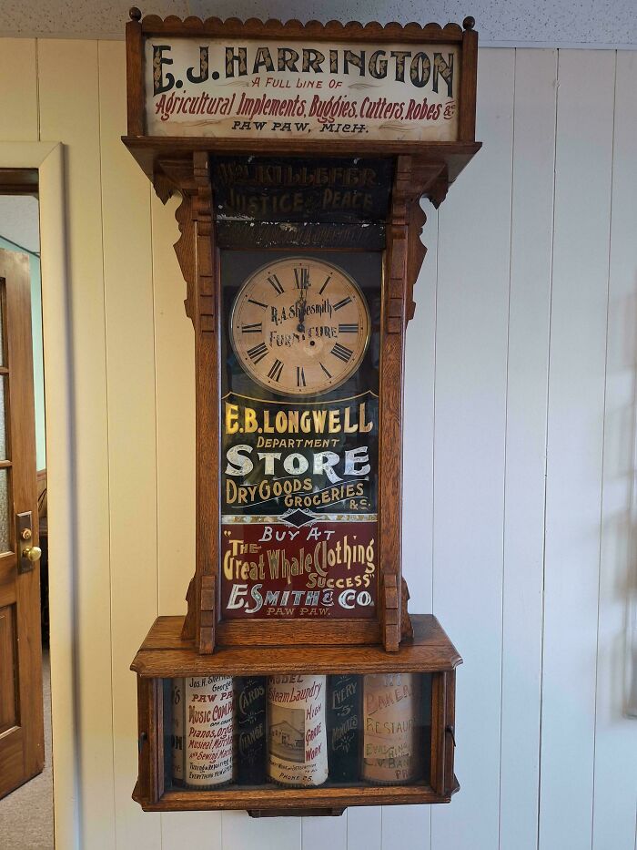Vintage wall clock with ornate woodwork and E.B. Longwell store advertising, showcasing classic typography and design.