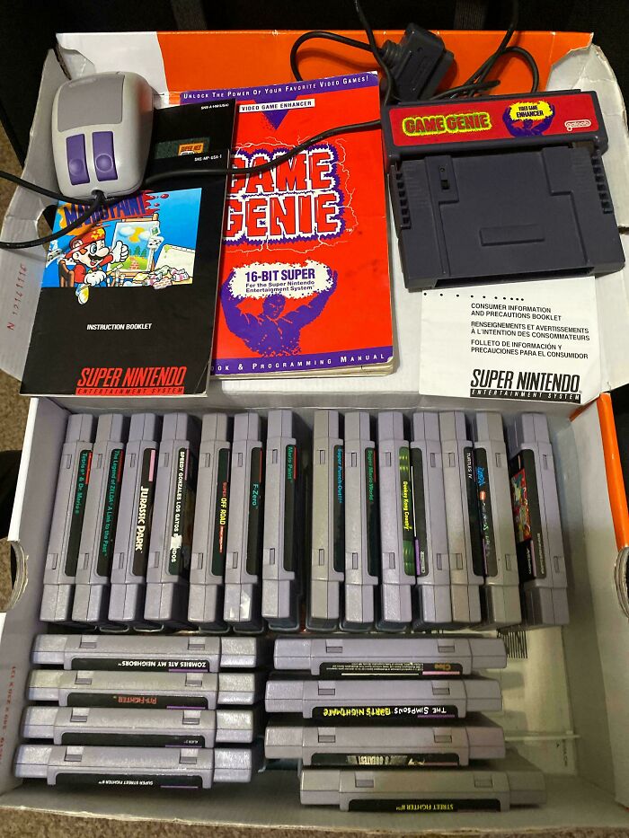 Vintage Nintendo game cartridges and manuals in a box with Game Genie accessory and mouse.
