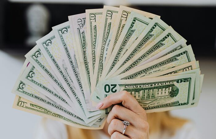 Person holding fanned-out US dollar bills, highlighting overused office expressions.
