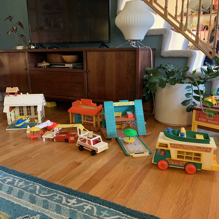 Vintage toys set on wooden floor, with colorful buildings and vehicles in a living room setting.