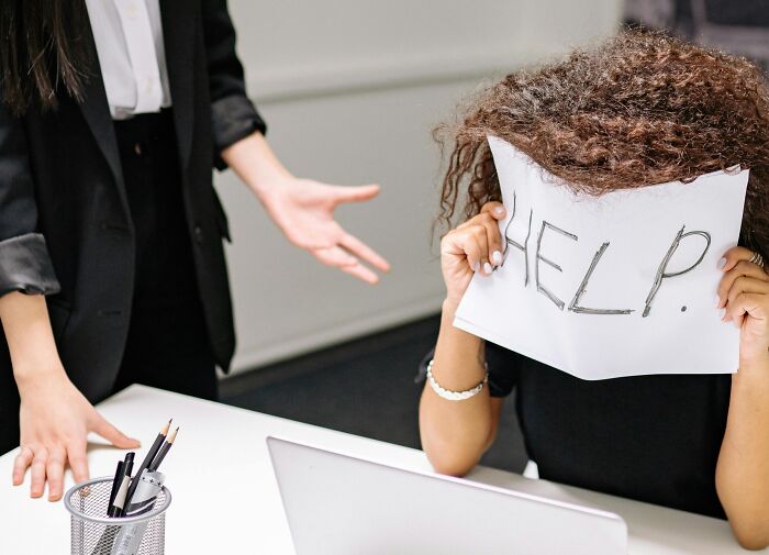 Person at desk holding "HELP" sign, illustrating dislike for overused office expressions.