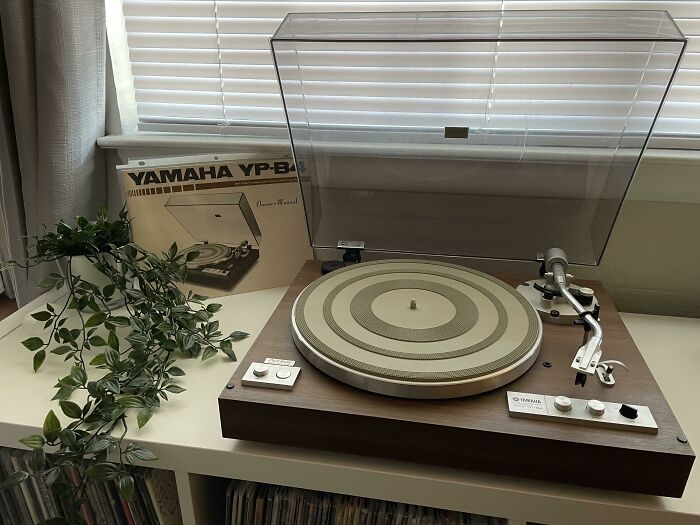 Vintage Yamaha YP-B4 turntable on a table with its manual, showcasing classic design elements against a window backdrop.