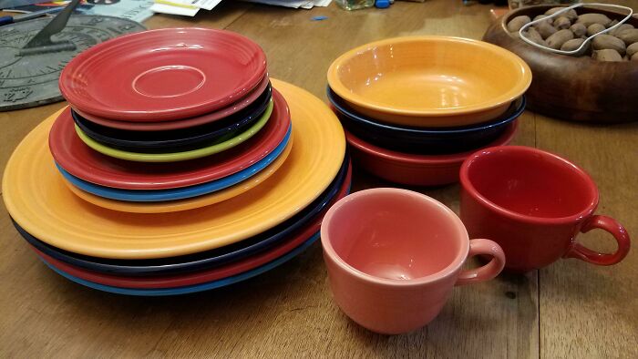 Vintage colorful dinnerware set on wooden table, featuring plates, bowls, and cups.