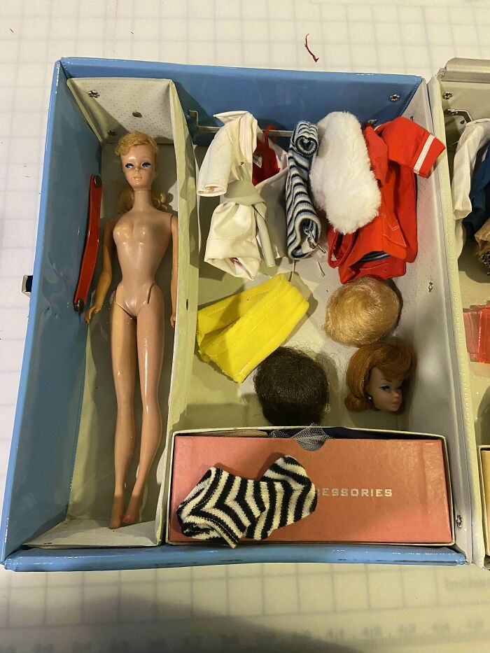 Vintage doll and accessories, including outfits and wigs, in a collectible case.