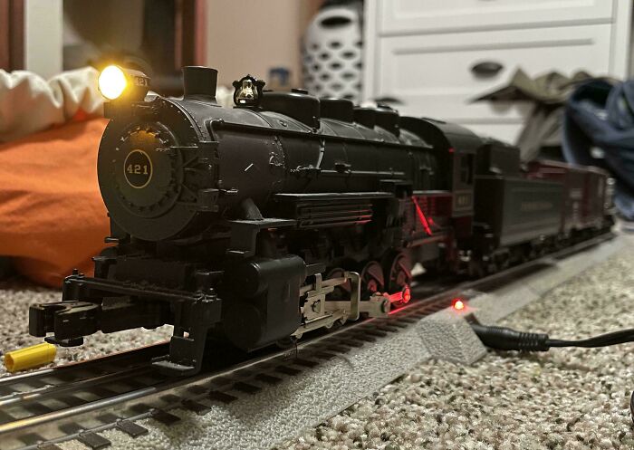 Vintage train set on carpeted floor, with a glowing headlight and detailed features.