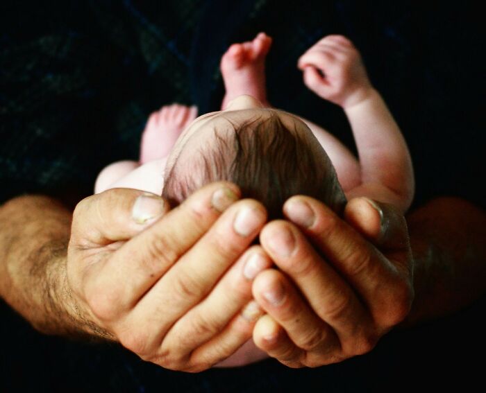 "Adult hands cradle a newborn baby, symbolizing care and innocence, touching on the dark side of history themes."