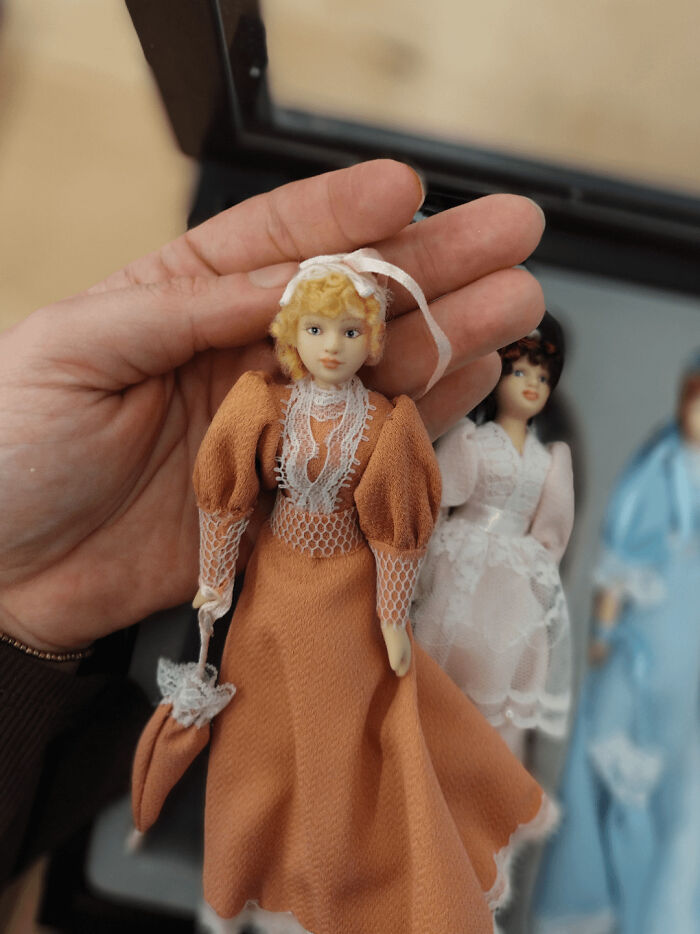 Hand holding vintage doll in orange dress, with two other dolls in background.