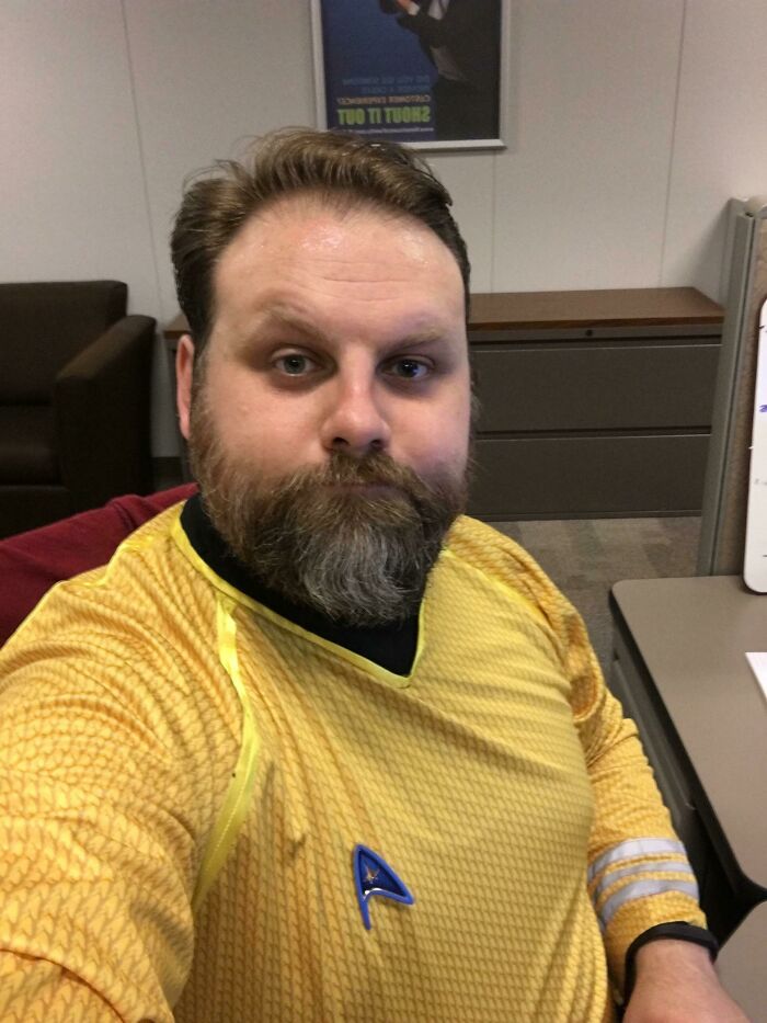 Man in yellow Star Trek uniform takes a selfie at his office desk, showcasing a unique colleague experience.
