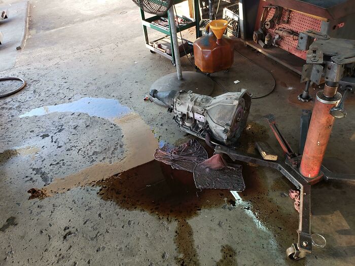 Workshop floor with an oil spill near automotive parts, showcasing a messy colleague's workspace.