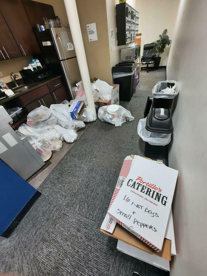 Office kitchen cluttered with trash bags and catering boxes, depicting worst colleagues' mess.