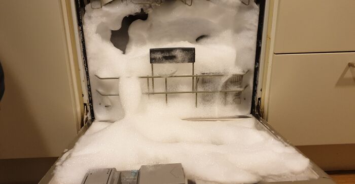 Dishwasher overflow caused by worst colleagues, with foam spilling out onto the kitchen floor.