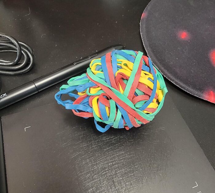 Rubber band ball on a desk near a pen and mouse pad, symbolizing chaos and bad colleagues at work.