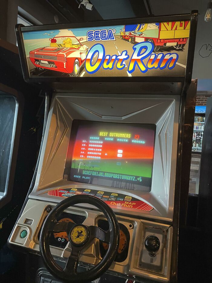 Vintage Sega OutRun arcade machine with steering wheel and screen displaying game leaderboard.