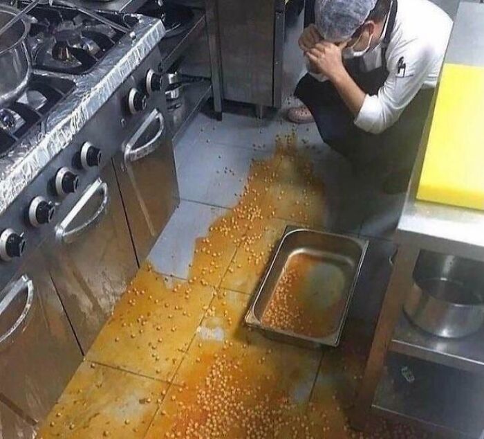 Kitchen worker crouches frustrated by spilled food on floor, showcasing a worst day at work scenario.