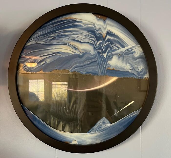 Round sand art piece with swirling blue and gold designs, creating an eye-catching display on the wall.