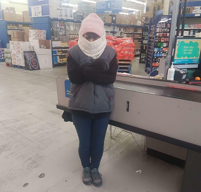Employee in winter gear at work, shivering behind a counter in a chilly store, illustrating a bad day at work.