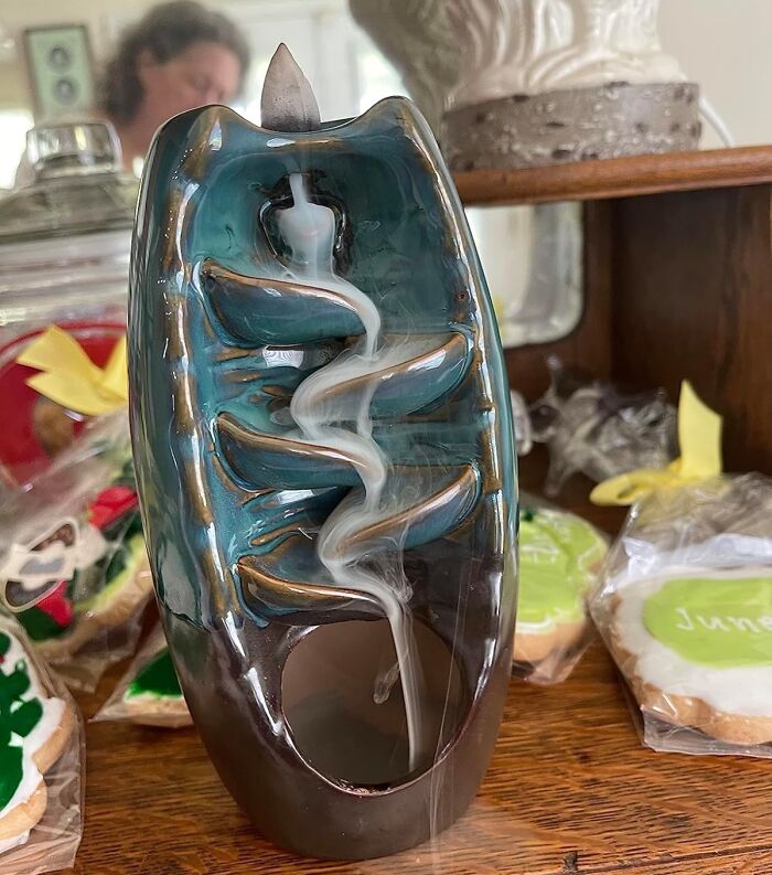 Decorative incense burner with flowing smoke in a creative design, placed on a wooden shelf.