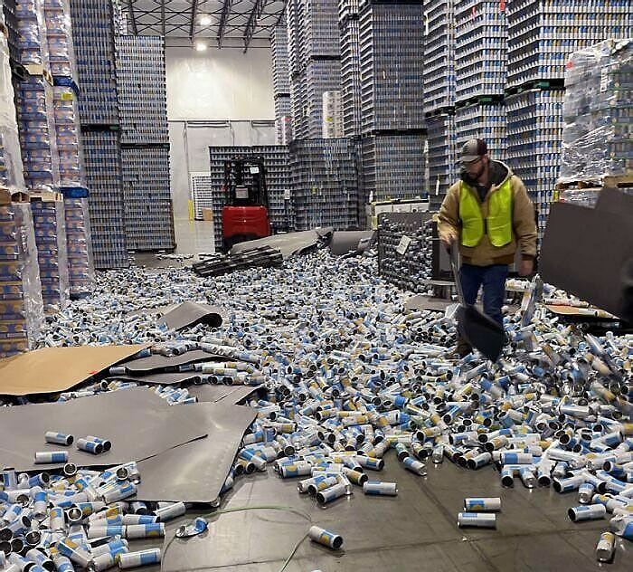 Worker dealing with fallen cans in a warehouse during worst day at work cleanup.