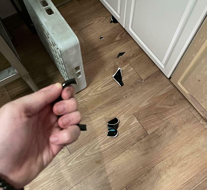 Broken mug on kitchen floor, hand holding handle, illustrating a worst day at work.