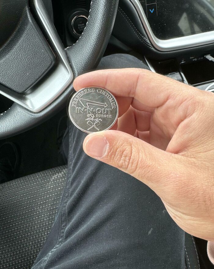 A hand holding a vintage In-N-Out Burger coin inside a car.
