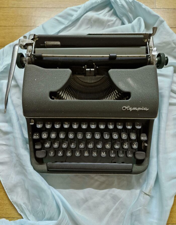 Vintage black Olympia typewriter on a light blue cloth, showcasing its classic keys and timeless design.