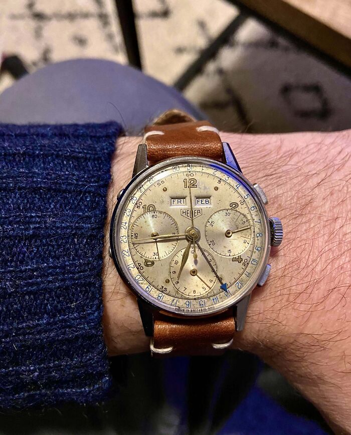Vintage Heuer watch with a tan leather strap, displaying day and month, on a wrist wearing a navy sweater.